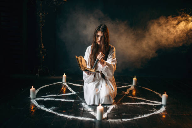istock Witch in white shirt holds knife and reads spell 946913284