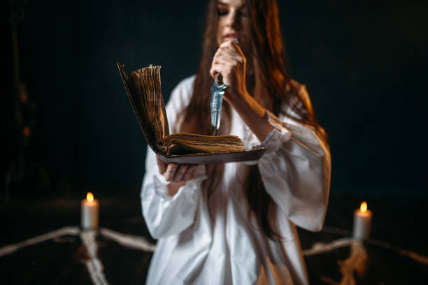 istock Witch in white shirt holds knife and reads spell 946913326
