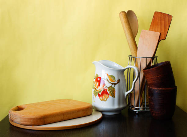 istock Kitchen utensils and dishware on dark table over yellow background. Kitchen interior background with copy space 946935082