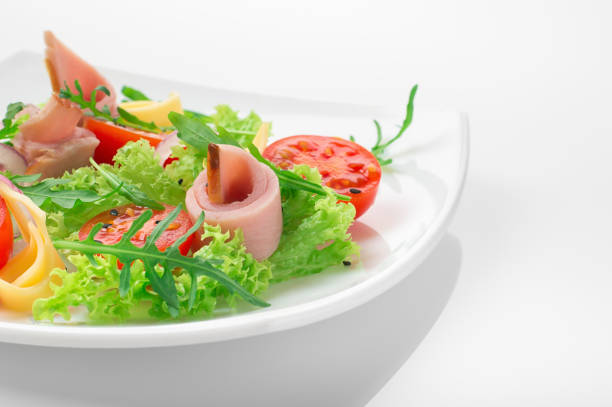 istock Fresh salad with tomatoes, arugula, cheese and ham on the white plate and white background 946935338