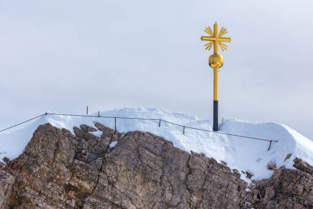 The golden cross on the top of Zugspitze mountain in the European Alps on a cloudy summer day.