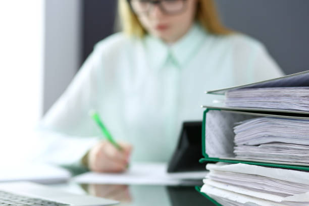 istock Bookkeeper or financial inspector  making report, calculating or checking balance. Binders with papers closeup. Audit and tax service concept. Green colored image backgroun 946941992