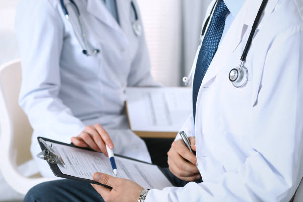 istock Two unknown doctors filling up medical form on clipboard, just hands closeup. Physicians asking question to patient or discussing medication program. Healthcare, insurance and medicine concept 946948392