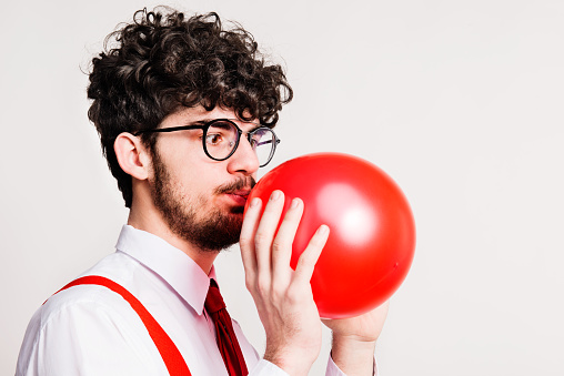 Portrait of a young handsome man blowing up a red balloon in a studio. Close up.