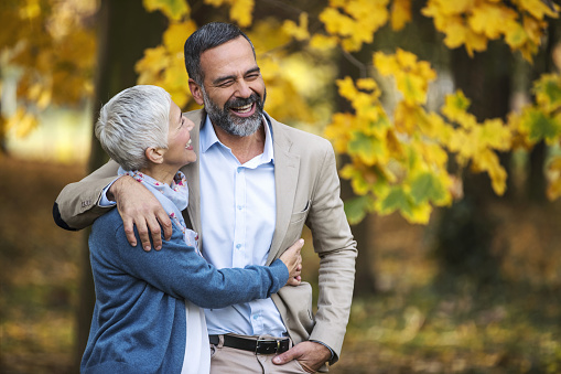 Closeup front view of early 50's couple having a relaxing walk in a park on a mild October day. They are walking between low branches with yellow leaves and laughing