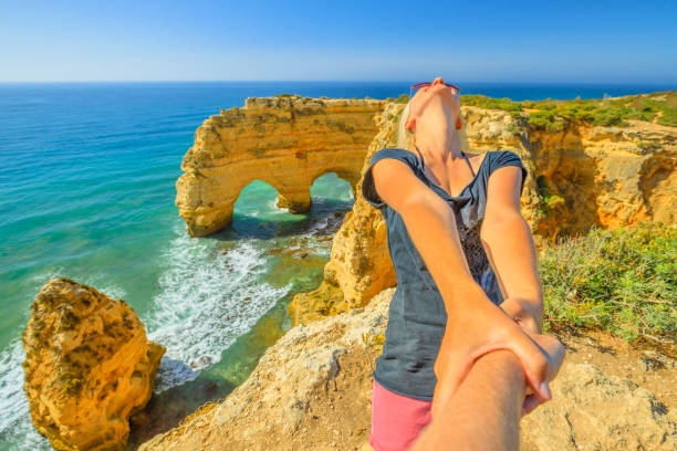 Follow me in Portugal Follow me, woman holding hands at natural arches of Praia da Marinha in Algarve, Portugal, Europe. Woman freedom at Marinha Beach. Concept of summer holidays and tourist traveler, holding man by hand. praia da marinha stock pictures, royalty-free photos & images