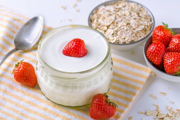 istock White yogurt in glass bowl with spoon and starwberries on white background. 946977652