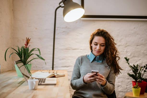 istock Beautiful smiling woman using her phone in modern home office. 946988400