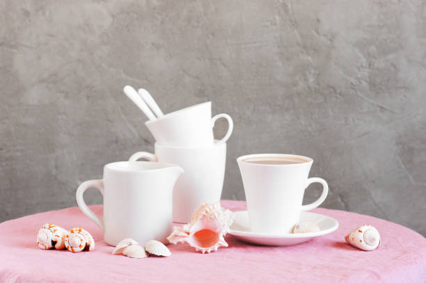 Life stile with white crockery for tea or coffee and shells on the table coated with pink tablecloth