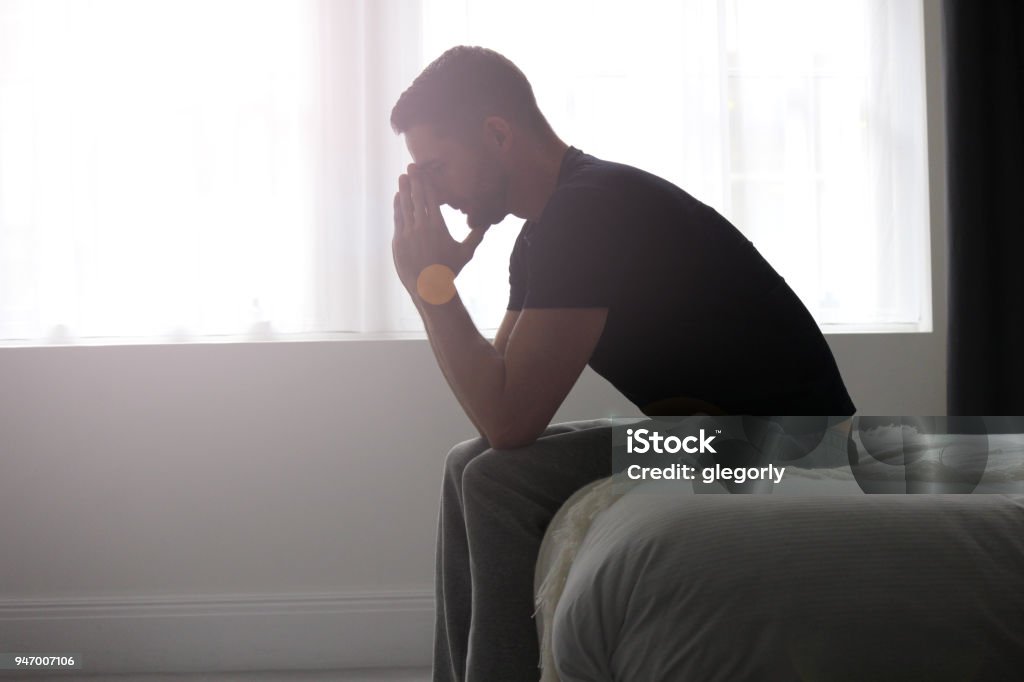 Depression A man sitting at the end of a bed, deep in solemn thought. Men Stock Photo