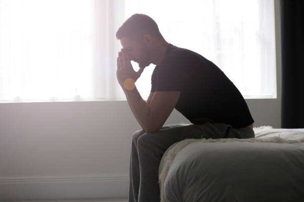 Depression A man sitting at the end of a bed, deep in solemn thought. brat stock pictures, royalty-free photos & images
