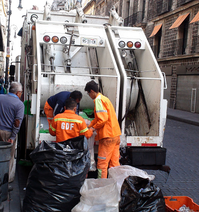 Scene Of Building Exterior, People Walking On The Street And Refuse Collectors Loading Garbage Into Garbage Truck In Mexico City Mexico