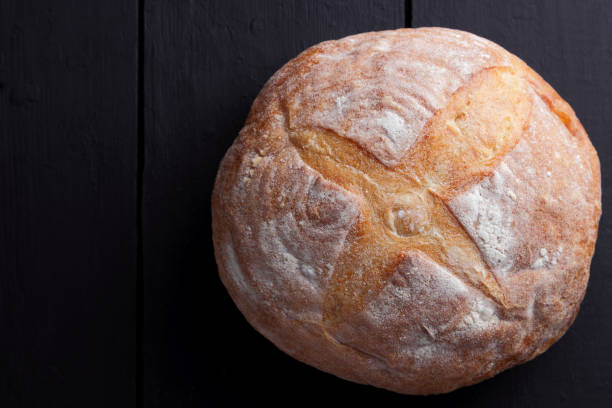 istock Round bread on a black background, bread from a stove on dark boards, a dough for a designer, copy space, rustic style, minimalism, top view, bakery 947017486