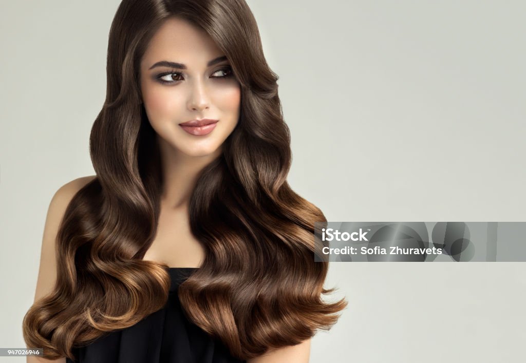 Young, brown haired beautiful model with long,curly, well groomed hair. Excellent hair waves. Young, brown haired woman  with curly and voluminous hair. Beautiful model with long, dense wavy hairstyle and vivid make-up. Perfect hair waves .Incredibly undulating and shiny hair. Hair Stock Photo