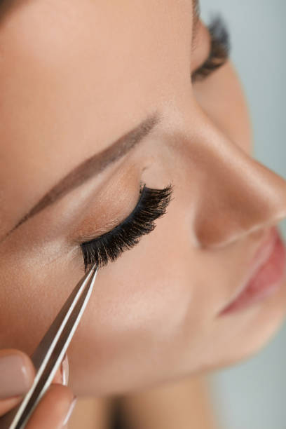 belleza maquillaje. mujer aplicación de pestañas postizas negro con pinza - applying make up flash fotografías e imágenes de stock