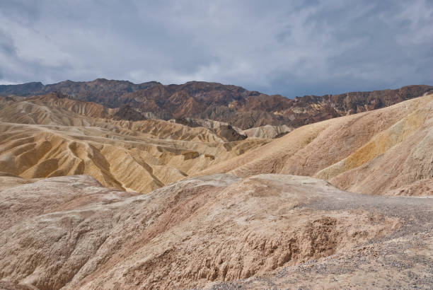 Badlands Formation Near Zabriskie Point The colorful landscape seen at Zabriskie Point extends several miles to the southeast. These spectacular multi-colored "badlands" formations may be viewed close up in Twenty Mule Team Canyon, a dry wash that winds through the undulating hills. The eroded formations have greatly contrasting colors - black or dark brown to the west, cream, yellow and white to the east. Zabriskie Point and Twenty Mule Team Canyon are in Death Valley National Park, California, USA. jeff goulden badlands stock pictures, royalty-free photos & images