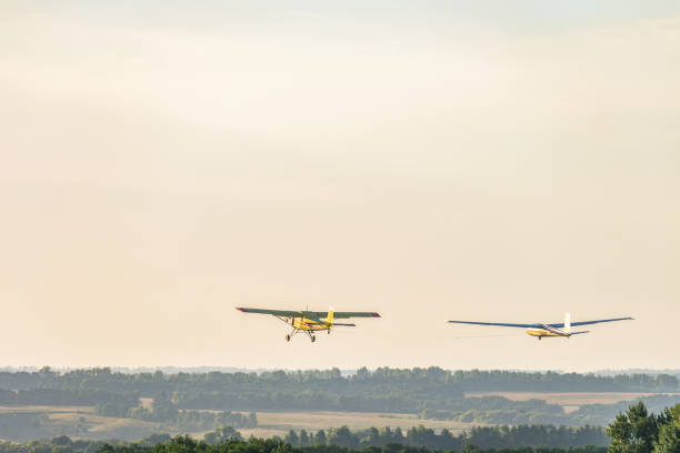 istock Small light-engine sport plane flying in the evening sky pulls on a rope the glider plane. Flight over the green hazy plain. 947045436