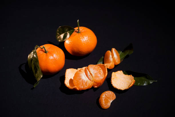 dos cítricos mandarina con cocimiento sobre fondo negro - leafes fruit orange leaf fotografías e imágenes de stock