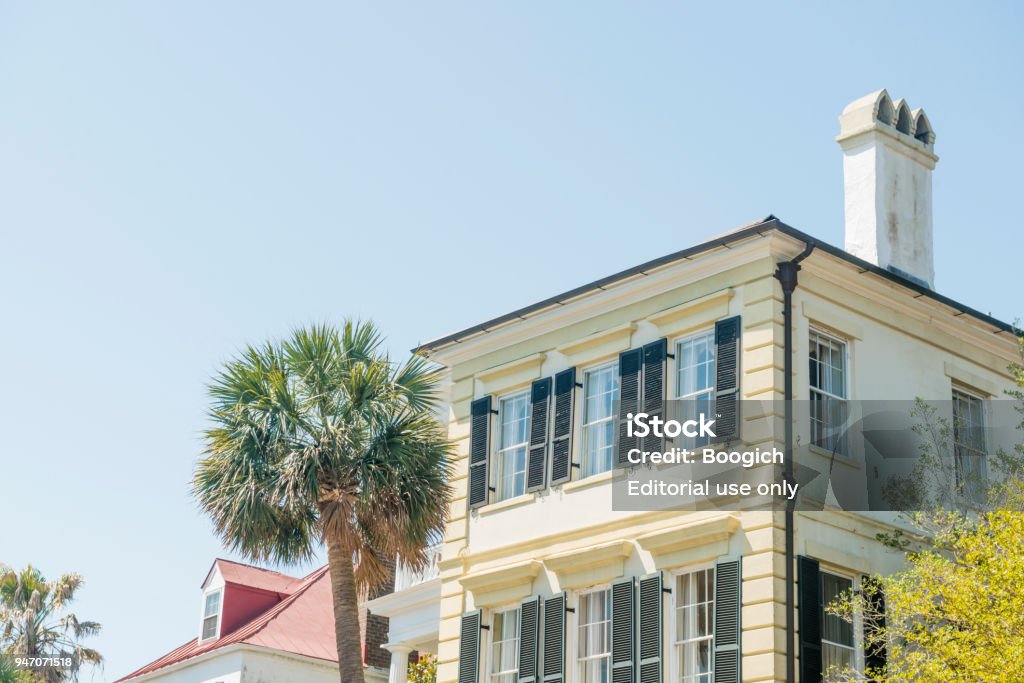 Historic Charleston Residential Home Architecture with Palm Tree South Carolina In Charleston, United States a tall palm tree grows alongside a historic residential home with open wooden shutters. Architecture Stock Photo