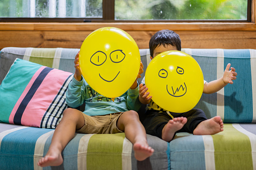 Kid holding Emoji face balloons and playing at home, in Auckland, New Zealand.