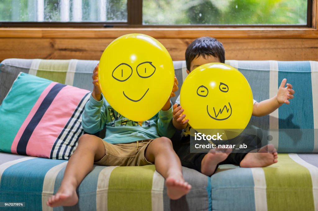 Two brothers playing with Emoji balloons. Kid holding Emoji face balloons and playing at home, in Auckland, New Zealand. Child Stock Photo