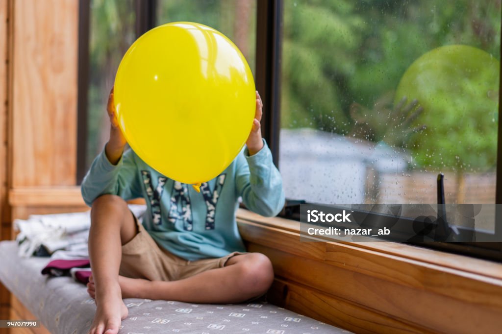 Kid covering face with love Emoji balloon. Kid holding Emoji face balloons and playing at home, in Auckland, New Zealand. 4-5 Years Stock Photo