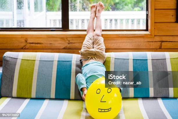 Kid Lying Upside Down On Sofa At Home And Covering Face With Balloon Stock Photo - Download Image Now