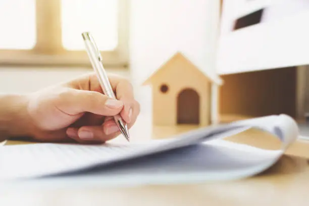 Photo of Close up hand of man signing signature loan document to home ownership. Mortgage and real estate property investment