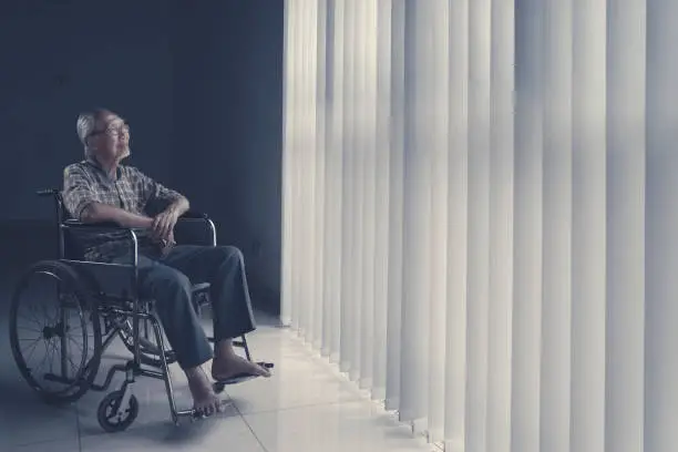 Elderly man sitting on wheelchair while looking at the window and smiling