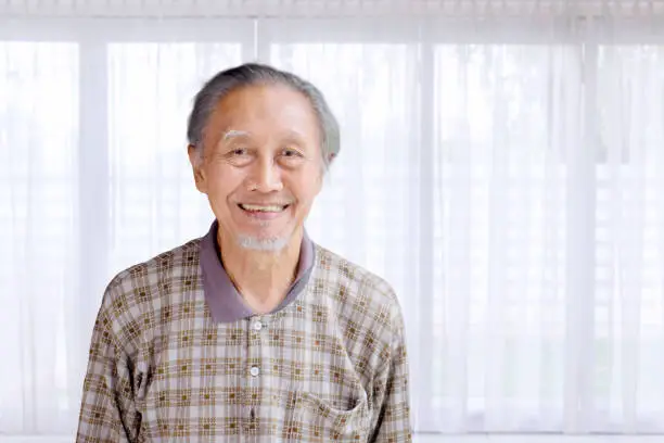 Portrait of Asian elderly man smiling at the camera near the window at home