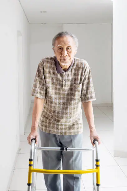 Portrait of lonely Asian elderly man walking with a walker at home