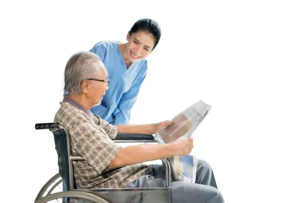 Young female nurse smiling at elderly man on wheelchair in the studio, isolated on white background