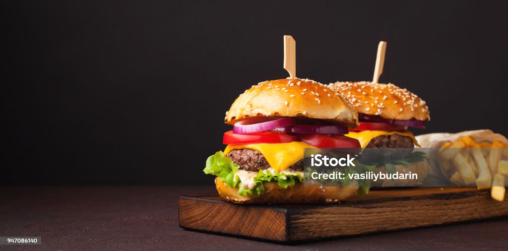 Primo piano di delizioso hamburger fresco fatto in casa con lattuga, formaggio, cipolla e pomodoro su sfondo scuro con spazio di copia. fast food e concetto di cibo spazzatura - Foto stock royalty-free di Hamburger di manzo