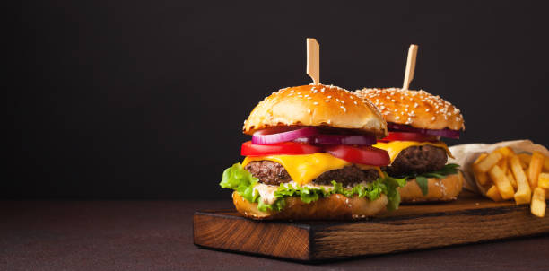Close-up of delicious fresh home made burger with lettuce, cheese, onion and tomato on a dark background with copy space. fast food and junk food concept Close-up of delicious fresh home made burger with lettuce, cheese, onion and tomato on a dark background with copy space. fast food and junk food concept. cheeseburger photos stock pictures, royalty-free photos & images