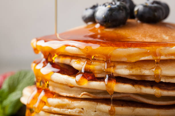 istock Close-up delicious pancakes, with fresh blueberries, strawberries and maple syrup on a light background. Sweet maple syrup flows from a stack of pancake 947088402