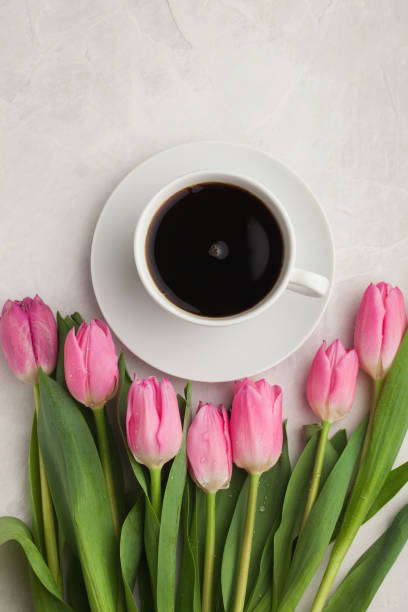 istock Black coffee in white Cup with pink tulips on light stone background. Top view 947088666