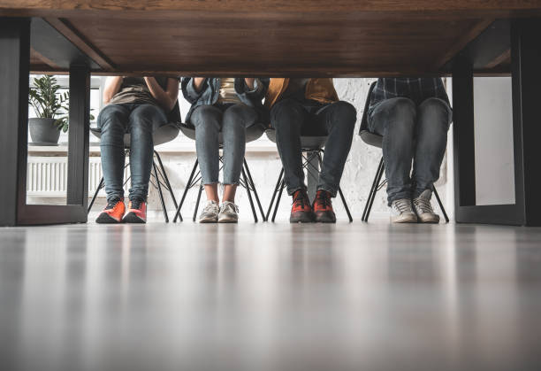 Young people having lesson indoors Four pair of legs sitting on chairs. Feet standing on floor together. Copy space table leg stock pictures, royalty-free photos & images