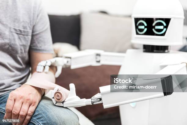 Hilfemedizinserviceroboter Setzt Einen Verband Auf Einem Arm Eines Männlichen Patienten Zu Hause Im Schlafzimmer Stockfoto und mehr Bilder von Roboter