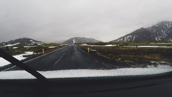Driving car through cold Iceland. Road is empty and peaceful, and you can really enjoy the time spend here. Path is clear, but you can see snow on the surrounding meadow and mountains. Iceland is great county for explorers and people ready for adventure.