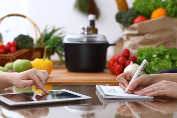 istock Closeup of human hands cooking in kitchen. Women discuss a menu using tablet computer. Copy space area at touch pad. Healthy meal, vegetarian food and lifestyle concepts 947133370