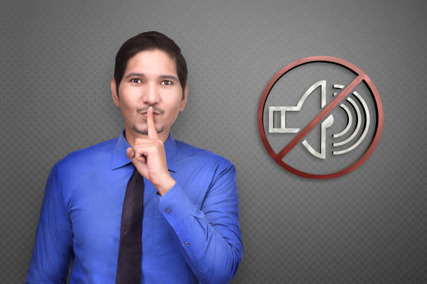 Young asian businessman with silence gesture and asking for quiet on gray background