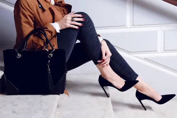 Photo of Close up legs woman in black high heels shoes sit on white stairs.