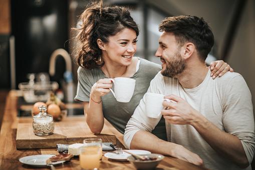 Young happy couple talking while drinking coffee in the morning. Focus is on woman.