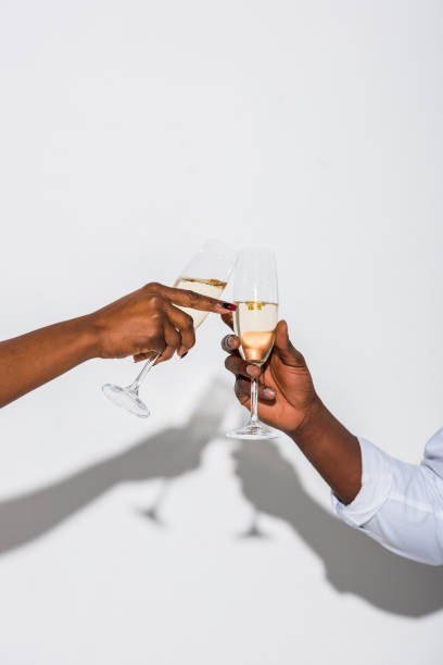 ritagliato colpo di coppia afroamericana clinking bicchieri di champagne su bianco - champagne celebration glass black foto e immagini stock