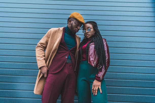 moda coppia afroamericana in giacca e cappotto in posa insieme all'esterno - street style foto e immagini stock