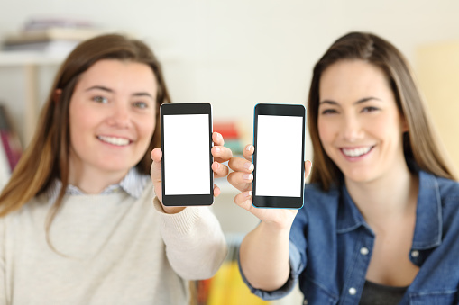Two happy students showing their both smart phone screens to camera at home