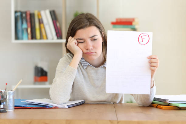 Sad student showing failed exam Sad student showing a failed exam to camera at home infamous stock pictures, royalty-free photos & images