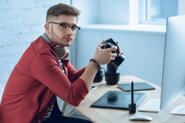istock Young photographer holding professional camera by working table 947189912