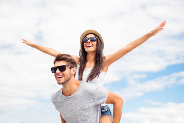 chico joven piggybacking novia alegre como el avión en el fondo del cielo - love couple city life urban scene fotografías e imágenes de stock