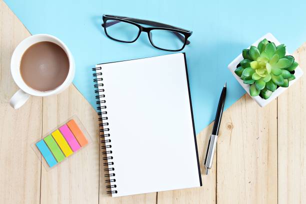 istock Top view or flat lay of open notebook with blank pages and coffee cup on office table 947202874